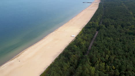 Aerial-shot-of-a-serene-sandy-beach-bordering-a-calm-sea-on-one-side-and-dense-green-forest-on-the-other