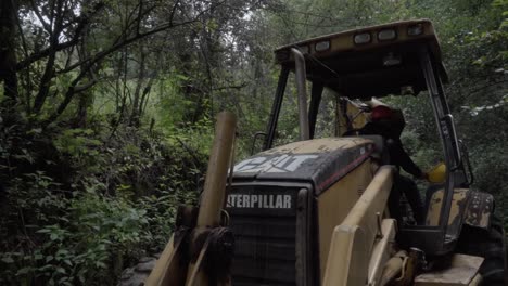 Un-Operador-Cambiando-Su-Casco-De-Seguridad-En-Una-Retroexcavadora-En-La-Vegetación.