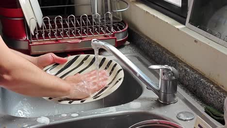 Man-rinses-his-hands-and-plates-while-he-watches-video-on-a-tablet