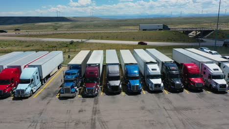 Aerial-tracking-shot-semi-trucks-parked-at-a-truckstop,-sunny-day-in-USA