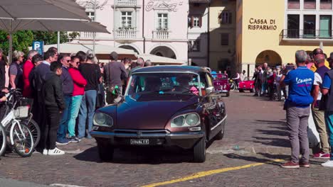 Oldtimer-Verlassen-Ihren-Treffpunkt-Am-Waltherplatz-In-Bozen,-Südtirol,-Während-Auf-Beiden-Seiten-Zuschauer-Stehen-Und-Den-Autos-Beim-Losfahren-Zusehen