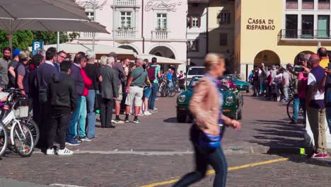 Oldtimer-Verlassen-Ihren-Treffpunkt-Am-Waltherplatz-In-Bozen,-Südtirol,-Während-Auf-Beiden-Seiten-Zuschauer-Stehen-Und-Den-Autos-Beim-Losfahren-Zusehen