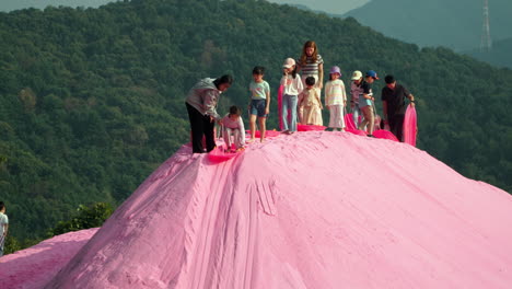 Herb-Island---Group-of-Children-Ride-Slider-Board-Sliding-Down-Pink-Sand-Hill-One-By-One---slow-motion