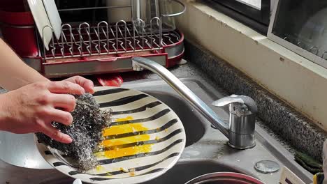 Man-scrubs-the-plates-with-steel-wool-while-he-watches-videos-on-a-tablet