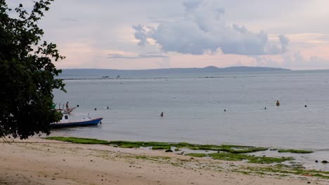 Scenic-landscape-view-of-people-swimming-and-playing-in-the-shallows-of-ocean-in-Kupang,-East-Nusa-Tenggara,-Indonesia,-Southeast-Asia