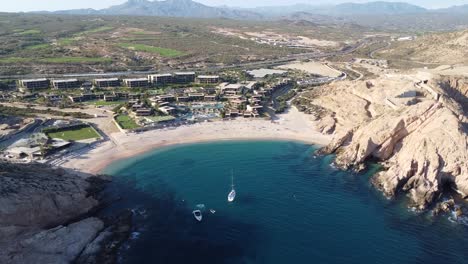 Aerial-view-over-the-gorgeous-santa-maria-beach-overlooking-the-clean-beach,-turquoise-waters-with-floating-sailboats-and-hoten-facilities-with-the-majestic-cliffs-and-mountains-in-the-background