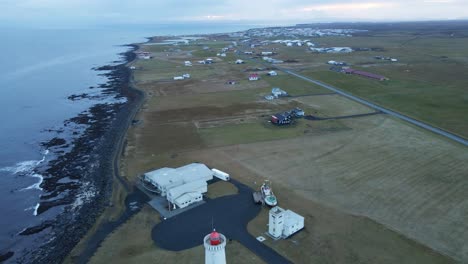 Drohne-Fliegt-über-Einen-Hohen-Leuchtturm-In-Richtung-Einer-Kleinen-Stadt-An-Der-Isländischen-Küste