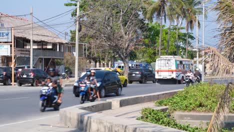 Local-traffic-with-colorful-district-bus,-yellow-taxi-and-other-vehicles-on-Pantai-Kelapa-street-in-capital-city-of-Dili,-Timor-Leste,-Southeast-Asia