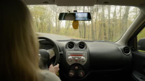 Woman-drives-car-narrow-autumn-tree-lined-country-road-backseat-view