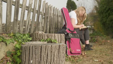 Girl-songwriter-musician-sits-writes-lyrics-rustic-picket-fence-scene