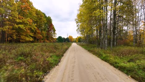 Moving-forward-down-a-country-dirt-road-in-late-autumn,-Fall-colors-in-the-trees