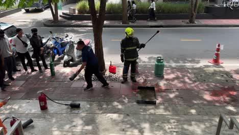 Firefighter-trainers-demonstrate-to-the-workers-the-correct-way-to-extinguish-fire-at-Saladaeng,-Bangkok,-Thailand