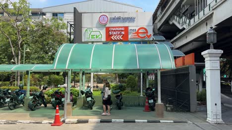 Blick-Auf-Die-Beschilderung-Der-Ladestation-Für-Elektroautos-Und-Die-Menschen,-Die-In-Der-Innenstadt-Von-Bangkok,-Thailand,-Spazieren-Gehen