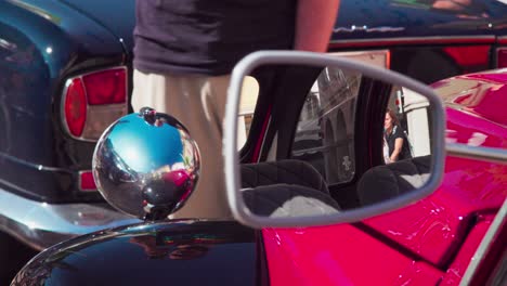 Side-mirror-and-back-of-front-light-of-a-vintage-Citroën-2CV-standing-behind-a-classic-Jaguar-during-a-classic-car-meeting-in-Bozen---Bolzano,-South-tyrol,-Italy