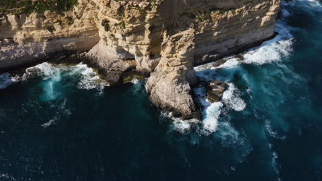 Aerial-view-of-steep-sunlit-cliffs,-on-the-coastline-of-sunny-Malta-island