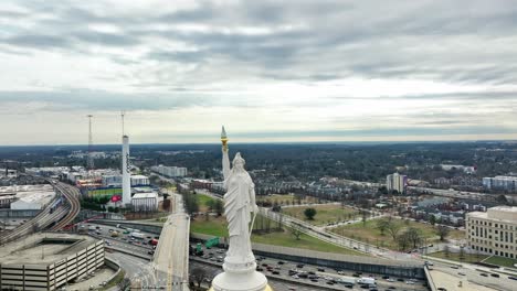 White-Statue-on-top-of-Georgia-Capitol-Museum-in-city-of-Atlanta-and-traffic-on-highway-at-cloudy-day---drone-orbit