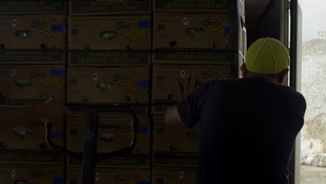 General-shot-of-worker-pushing-boxes-of-bananas-into-a-truck,-customs