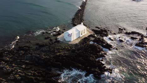 White-chapel-on-tiny-rocky-island-in-Crete,-aerial-orbit-view