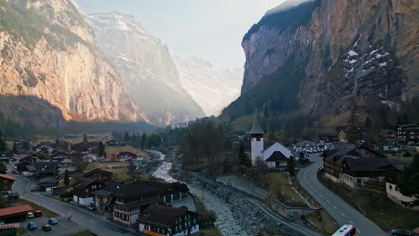 Idyllic-peaceful-town-between-canyon-walls-with-river-winding-below-church-and-homes,-Lauterbrunnen,-Switzerland