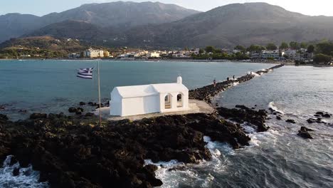 Weiße-Kapelle-Mit-Griechischer-Flagge-In-Georgiopoli,-Kreta,-Luftaufnahme