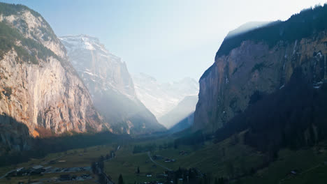 Aerial-establishing-view-of-valley-in-Lauterbrunnen,-Switzerland-as-sunlight-crests-over-mountain-ridge