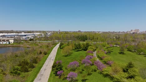 Aerial-flyover-idyllic-Liberty-State-park-with-walking-person-in-spring-season-during-sunny-day,-NYC