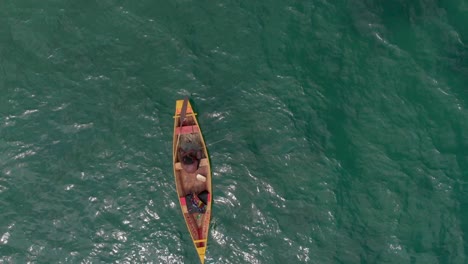 Black-man-sitting-shirtless-on-boat-rowing-it-in-the-blue-river-waters