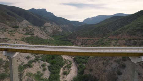 Elevated-bridge-in-Oaxaca,-Mexico-with-mountainous-backdrop-and-winding-dry-river---Aerial