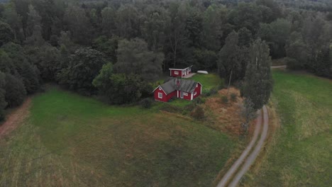 Reveal-shot-of-red-Swedish-house-surround-by-nature,-aerial
