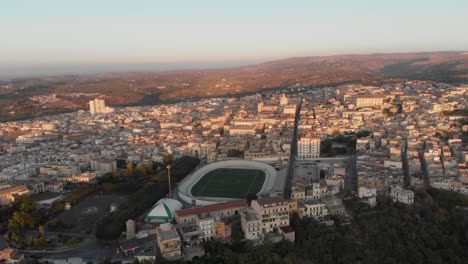 Aerial-view-of-city-of-Noto-with-soccer-field-during-sunrise,-Sicily