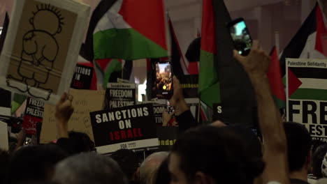 En-Cámara-Lenta,-Una-Multitud-Abarrotada-De-Personas-Sostiene-Pancartas-Y-Banderas-Durante-Una-Protesta-Pro-palestina-Frente-A-La-Embajada-De-Israel-Al-Atardecer.