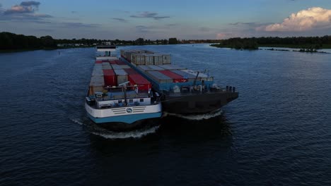 Tieffliegende-Drohnenansicht-Von-Frachtschiffen-Mit-Containern,-Die-Gemeinsam-Auf-Niederländischen-Flüssen-Segeln-Und-Fracht-Liefern