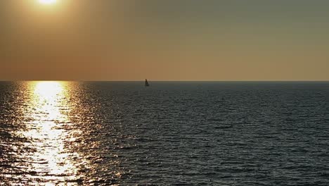 Sail-boat-sailing-far-away-in-open-sea-at-sunset