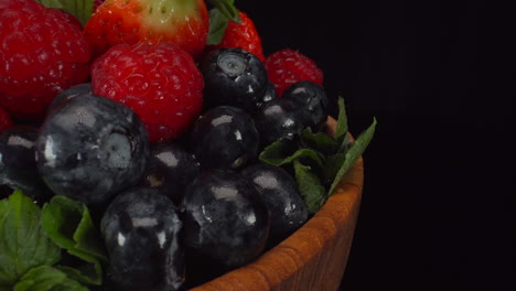 Rotating-fresh-forest-berries-in-a-wooden-bowl,-wet-bright-fruits,-strawberries,-blueberries,-raspberries,-4K-macro-shot