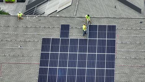 Luftaufnahme-Von-Arbeitern,-Die-Solarpaneele-Auf-Einem-Schindeldach-Installieren,-Wobei-Die-Paneelreihen-Bereits-Angebracht-Sind