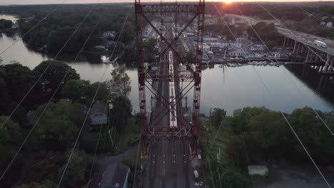 Overhead-Drone-Shot,-Pan-Down,-Commuter-Train-Passing-Below-at-Sunset