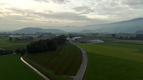 Toma-Aérea-De-Establecimiento-De-Una-Carretera-En-Una-Zona-Rural-De-Suiza-Con-La-Ciudad-De-Bilten-Al-Fondo