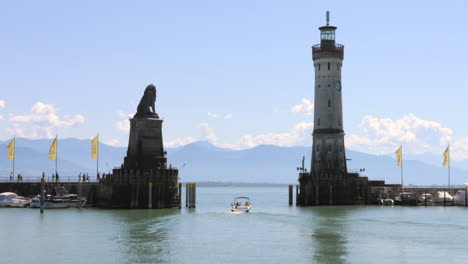 Small-boat-sails-out-of-old-Lindau-harbor,-between-lighthouse,-Bavarian-lion-statue