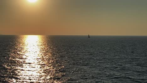 Sail-boat-sailing-far-away-in-open-sea-at-sunset