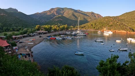 Zoom-in-of-Girolata-beach-and-small-harbor-with-moored-boats-and-people-on-vacation-in-summer-season-at-sunset
