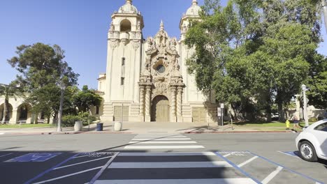 Casa-del-Prado-Balboa-park-San-Diego-California,-with-pedestrian-crossing,-trees-and-a-runner-passing
