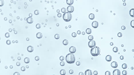 Water-bubbles-with-white-background,-camera-tilting-up-along-the-bubbles-as-some-bubbles-start-to-move-up-towards-the-surface