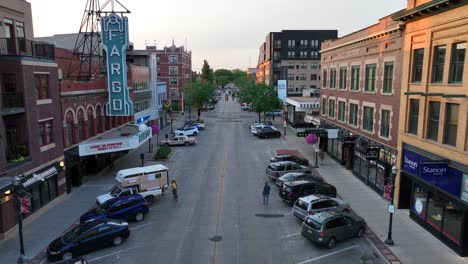 Fargo-Theater's-iconic-sign-stands-tall-amidst-historic-brick-buildings,-overlooking-a-bustling-downtown-street-lined-with-parked-cars-at-sunset