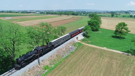 An-Aerial-From-Ahead-View-of-a-Steam-Passenger-Train,-Traveling-Thru-Harvested-Farmlands-on-a-Sunny-Day-in-Slow-Motion