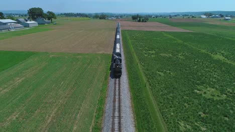 An-Aerial-Head-On-Above-View-of-a-Steam-Passenger-Train-Approaching,-Traveling-Thru-Harvested-Farmlands-on-a-Sunny-Day-in-Slow-Motion