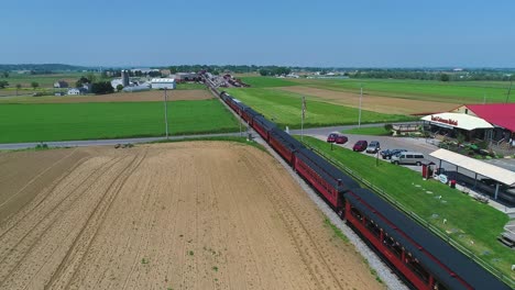 An-Aerial-Head-From-Behind-View-of-a-Steam-Passenger-Train,-Traveling-Thru-Harvested-Farmlands-on-a-Sunny-Day-in-Slow-Motion