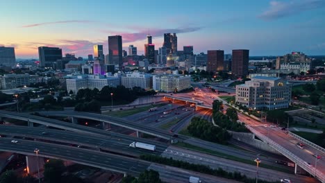 Vista-Aérea-Del-Horizonte-De-La-Ciudad-De-Atlanta-Y-El-Tráfico-En-La-Autopista-De-Cruce-Durante-La-Puesta-De-Sol-Dorada