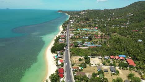 Aerial-flyover-coastal-road-with-traffic-beside-turquoise-ocean-on-Koh-Samui,-Thailand-at-sunny-day