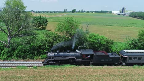 An-Aerial-Side-View-of-a-Steam-Passenger-Train,-Stopped-Traveling-Thru-Harvested-Farmlands-on-a-Sunny-Day-in-Slow-Motion