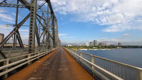 Bike-path-on-metal-bridge-with-city-skyline-and-river-backdrop,-Canada